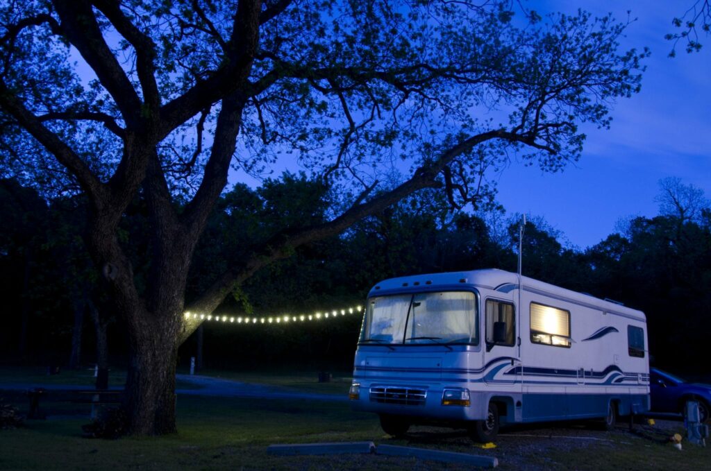 an RV with interior lights on and an exterior string of lights during the night