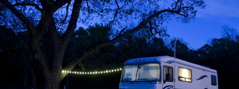 an RV with interior lights on and an exterior string of lights during the night